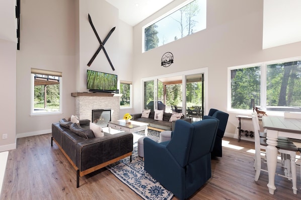 A spacious living room with a fireplace, a television, and a large window overlooking a forest.