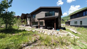 Ett modernt hus i två våningar med en täckt uteplats, omgivet av en naturlig landskap och andra bostadshus.