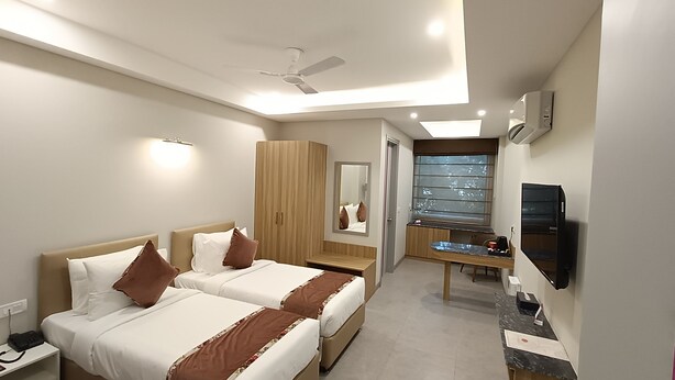 A hotel room with two beds, a desk, a mirror, a window, and a ceiling fan. - ROSASTAYS Gurugram Sec 31 (Gurugram)
