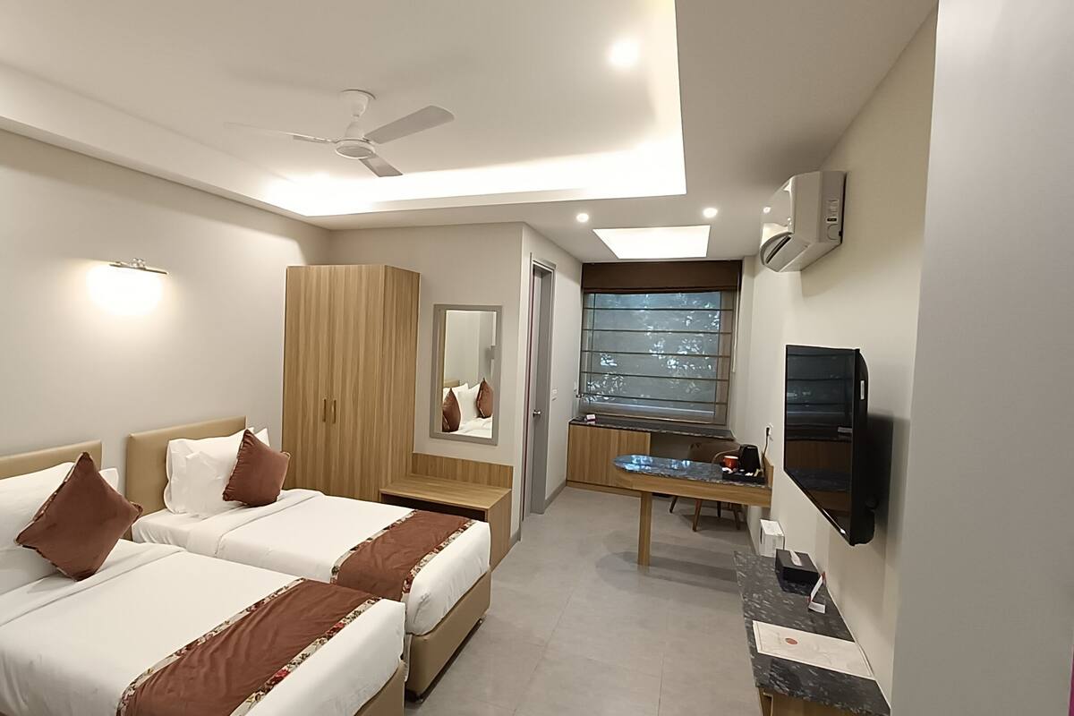 Habitación de hotel con dos camas, un escritorio, un espejo, una ventana y un ventilador de techo.