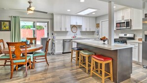 A modern kitchen with white cabinets, a central island with stools, a dining table with chairs, and a ceiling fan. - San Marcos Home w/ Patio & Grill - Walk to Lake! (San Marcos)