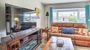 A living room with a large flat-screen TV, leather sofa, wooden entertainment unit, and a view through a large window. - San Marcos Home w/ Patio & Grill - Walk to Lake! (San Marcos)