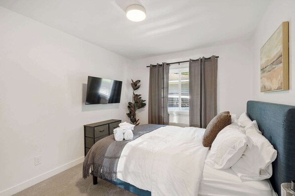 A bedroom with a bed, a TV mounted on the wall, a bedside table, and a window with curtains. - Newly Updated 1 BR Flat Near Downtown A2 (Ann Arbor)