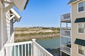 Un balcon avec vue sur une plage, une étendue d’eau et des bâtiments situés au loin.