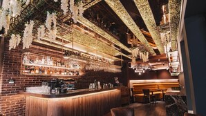 Eine Barbereich mit Backsteinwand, Holztresen und hängenden weißen Blumen.