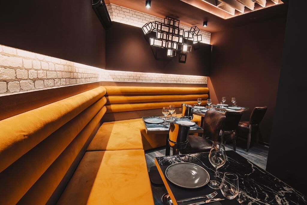 A restaurant with booth seating and a brick wall. Tables are set with plates, glasses, and cutlery.