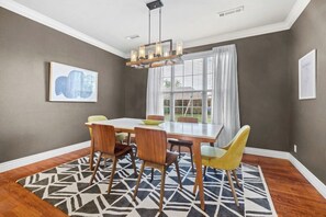 A dining room with a rectangular table, four chairs, a patterned rug, and a chandelier.