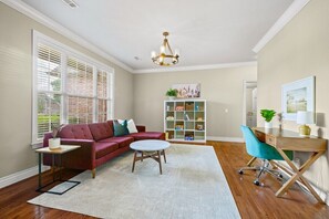 Un salon avec un canapé rouge, une table basse blanche, une bibliothèque et un bureau avec une chaise.