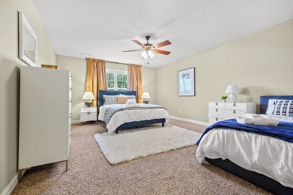 A bedroom with a bed, a nightstand, a dresser, a ceiling fan, and a window with curtains.