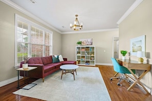A living room with a red sofa, a white coffee table, a bookshelf, and a desk with a chair.