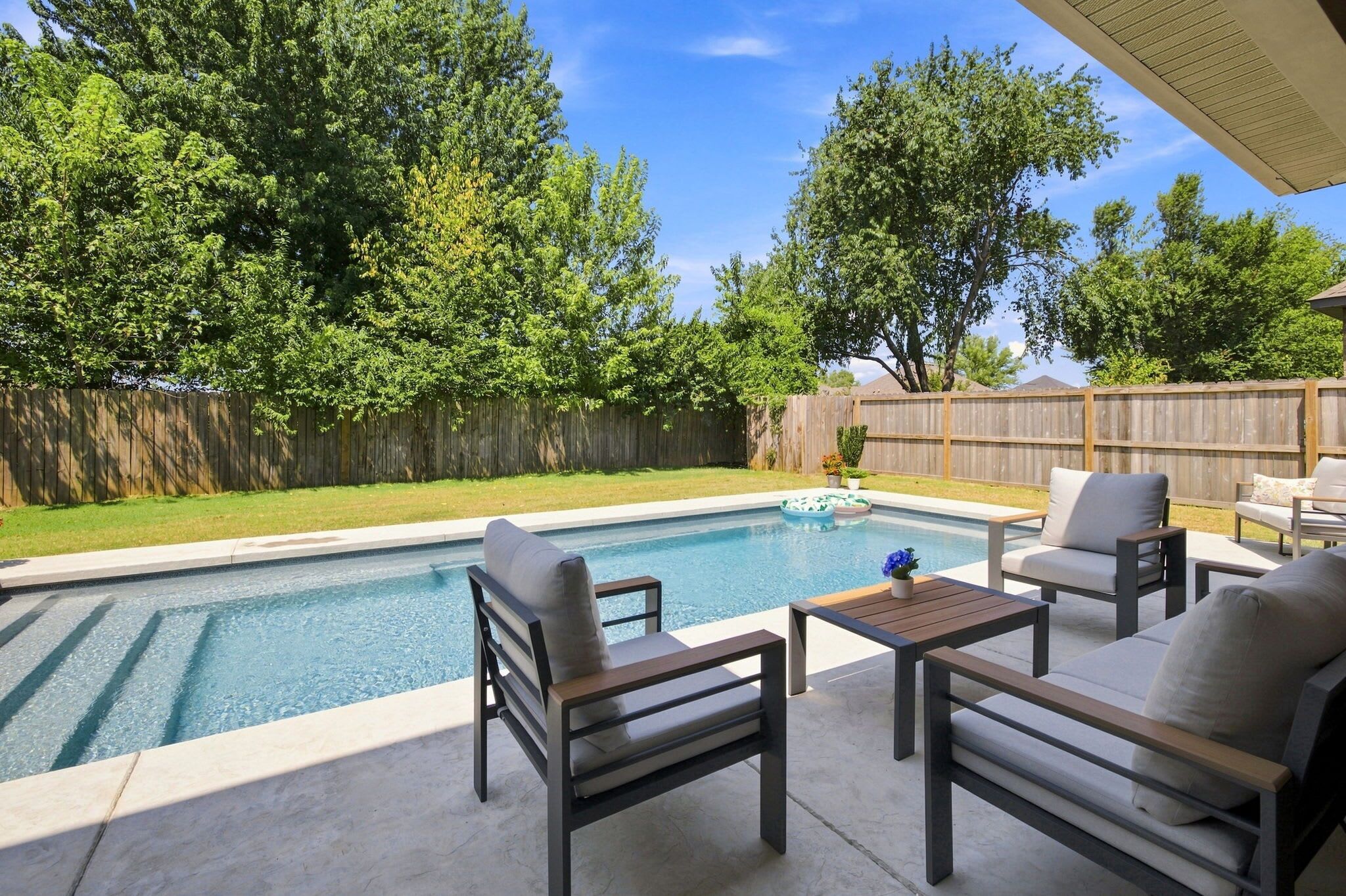 Un jardin avec une piscine, des meubles de patio et une clôture en bois.