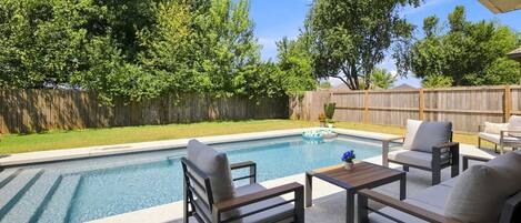 Un patio trasero con piscina, mobiliario de jardín y un cerco de madera.