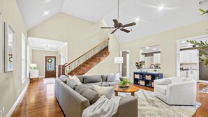 Un salon spacieux avec un escalier en bois, un canapé d’angle gris, un fauteuil blanc et une table basse.