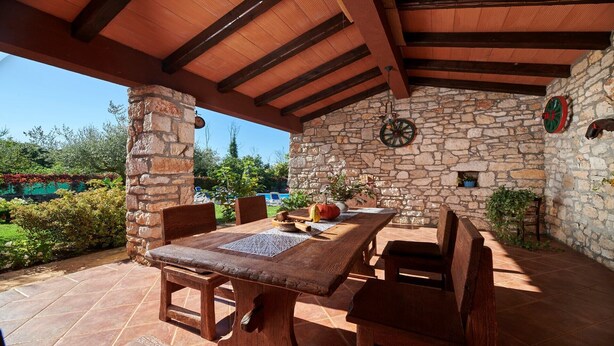 Un patio al aire libre con pared de piedra, muebles de madera y un ambiente rústico.