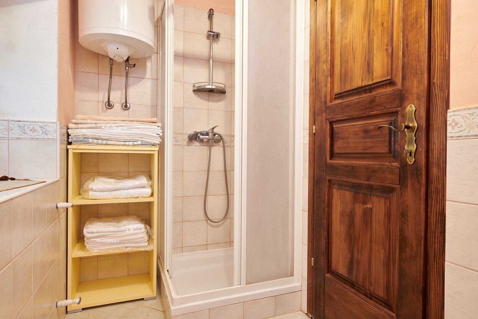 Une salle de bain avec une porte en bois, une douche équipée d’un pommeau de douche à main et une étagère avec des serviettes pliées.