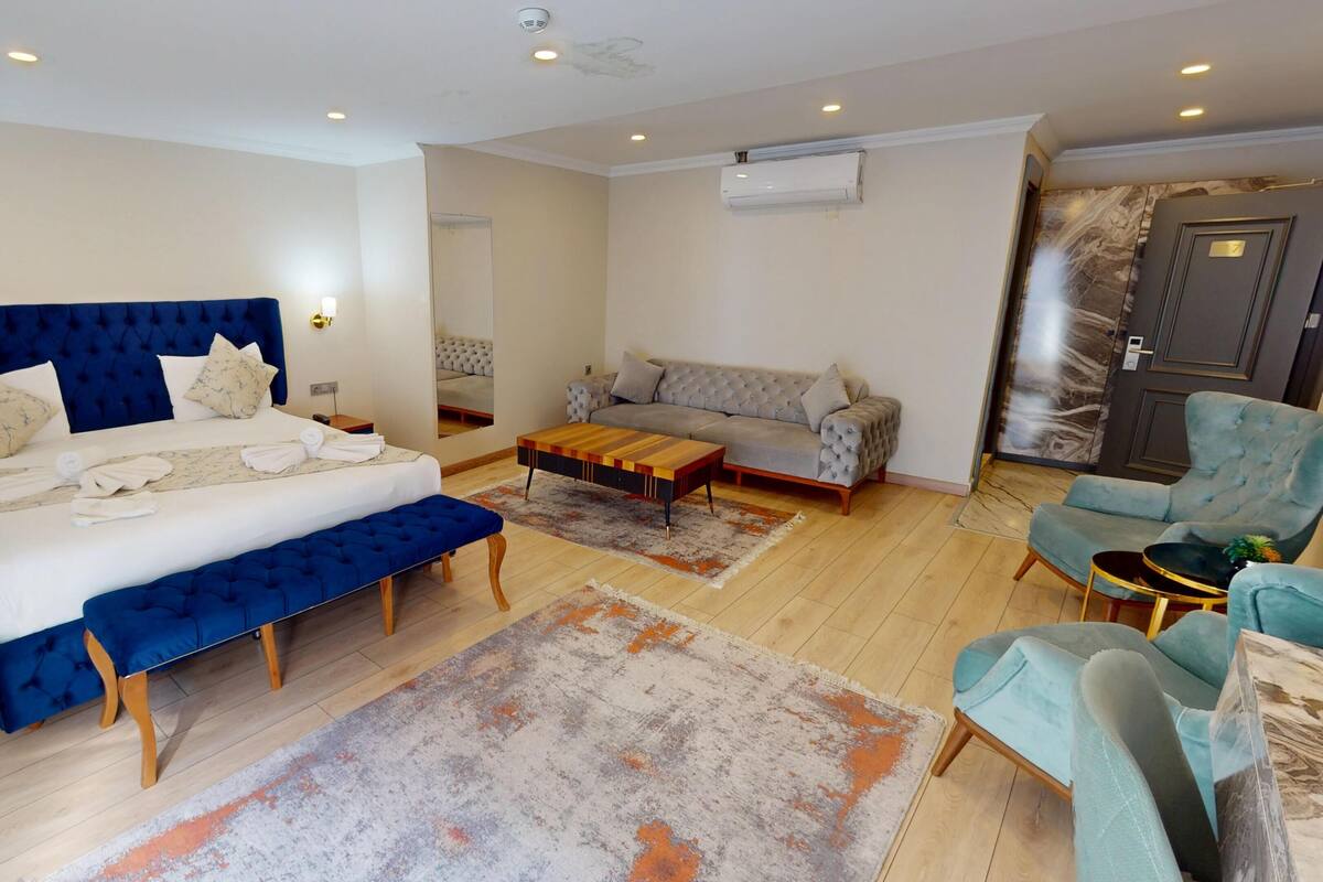 Une chambre d’hôtel avec un grand lit, un canapé, un fauteuil, une petite table et un appareil de climatisation.