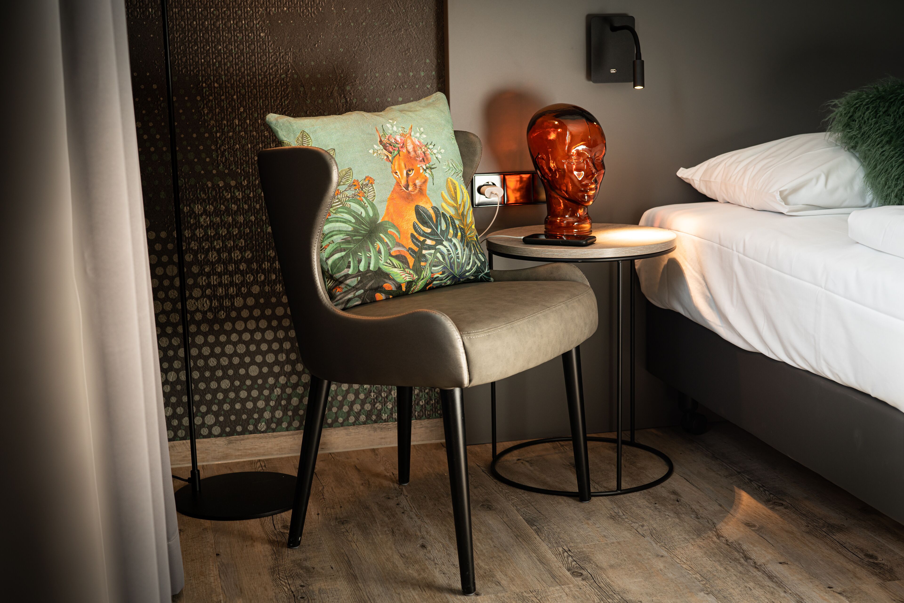 Una habitación moderna con una cama, una silla, una mesita pequeña y una escultura decorativa.