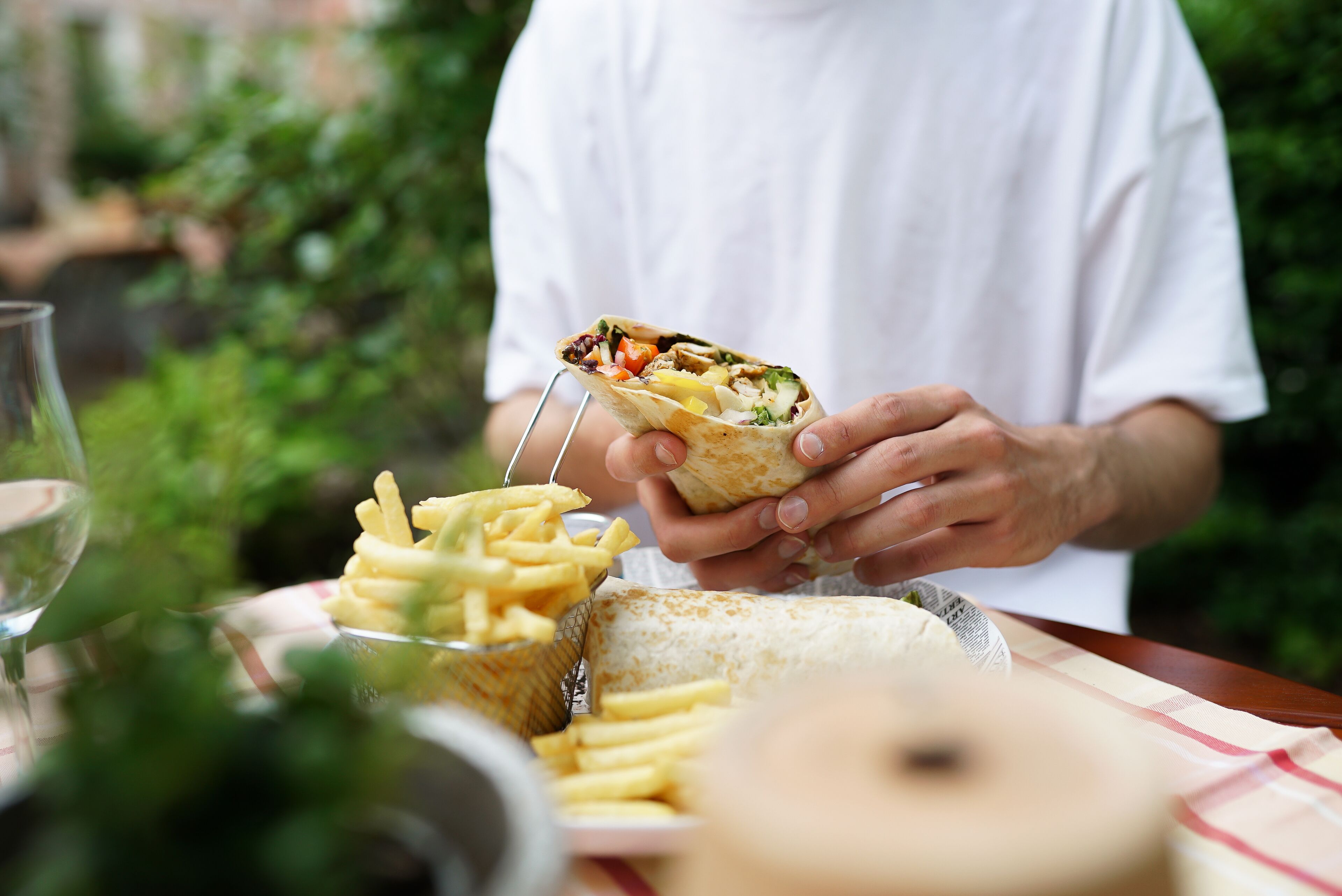 Una persona sosteniendo un wrap de verduras y una porción de papas fritas.