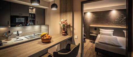 A modern hotel room with a kitchenette, a dining area, and a bed.
