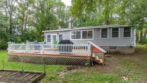 Situated in a wooded area, this home offers a covered deck with a white railing and steps leading up to it.