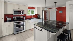 A modern kitchen with white cabinetry, stainless steel appliances, and a black marble island. - Cozy Colchester Cabin near Lake by RedAwning (Colchester)