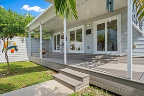 Steps lead up to a covered porch with white columns and flat roof, surrounded by a well-manicured lawn.
