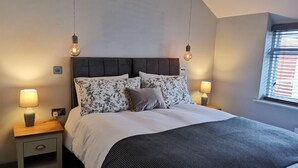 A neatly made bed with floral pillows, two bedside lamps, and a window with blinds.