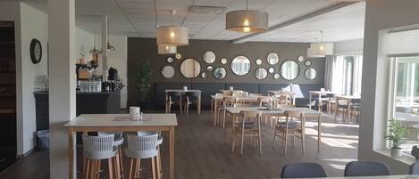 Ein modernes Café mit mehreren Tischen und Stühlen, verschiedenen Spiegeln an der Wand und einem großen Fenster, das natürliches Licht hereinlässt.