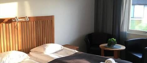 Habitación de hotel con una cama grande, una mesita pequeña, una silla y una ventana con cortinas.