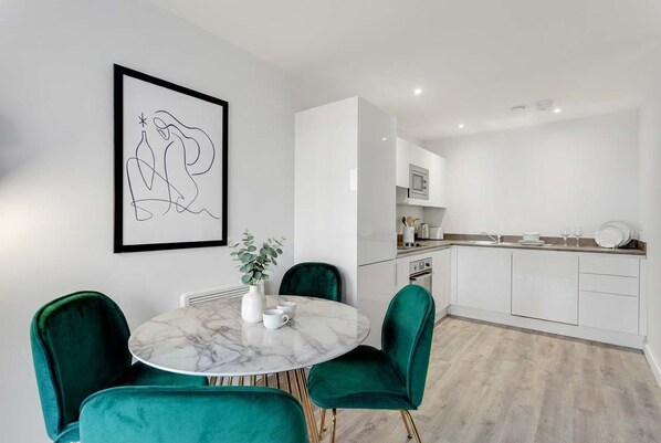 A modern kitchen with white cabinets, a marble table, and green chairs.