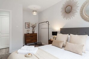 A bedroom with a bed, bedside table, lamp, and a wall-mounted mirror.