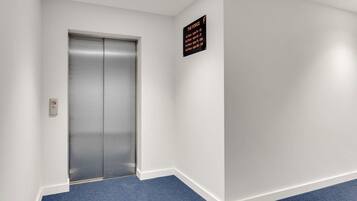 A hallway with a blue carpet, a closed elevator, and a sign listing floor names and numbers.