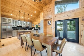 Un interior de madera espacioso con una gran mesa de comedor, electrodomésticos de cocina modernos y vistas a través de la puerta de vidrio.
