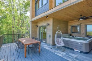 A wooden deck with a table and chairs, a hot tub, and a hanging chair.