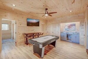 A wooden interior with a pool table, bar stools, and a ceiling fan.