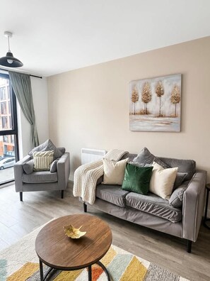 A modern living room with a grey sofa, a smaller armchair, a round coffee table, and a painting on the wall.