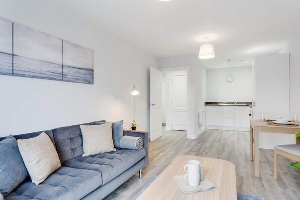 A modern living room with a sofa, a coffee table, and a kitchen in the background. - Modern & Spacious 1 Bed Flat In Central Birmingham (Birmingham)