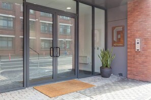 A modern building entrance with glass doors, a potted plant, a doormat, and a sign that reads 'The Foundry.'