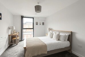 A bedroom with a bed, bedside tables, a lamp, a window, and a view of buildings outside.