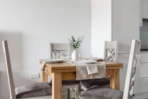 A dining table with chairs, a vase with greenery, and a white wall.