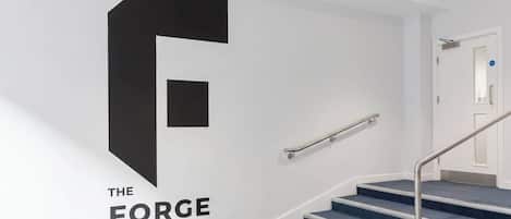 A staircase with a large black letter 'F' and the words 'THE FORGE' on the wall, leading to a door with a blue carpeted landing.