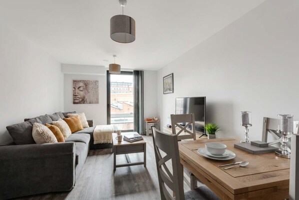 A modern living room with a sofa, dining table, and chairs, a TV, and a window with a view.