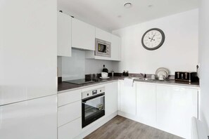 A modern kitchen with white cabinetry, a microwave, an oven, a clock, and a toaster.