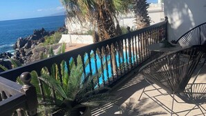 A balcony with a view of the ocean, a palm tree, and a white building in the background. - 3 bedroom ocean shore apartment (Santiago del Teide)