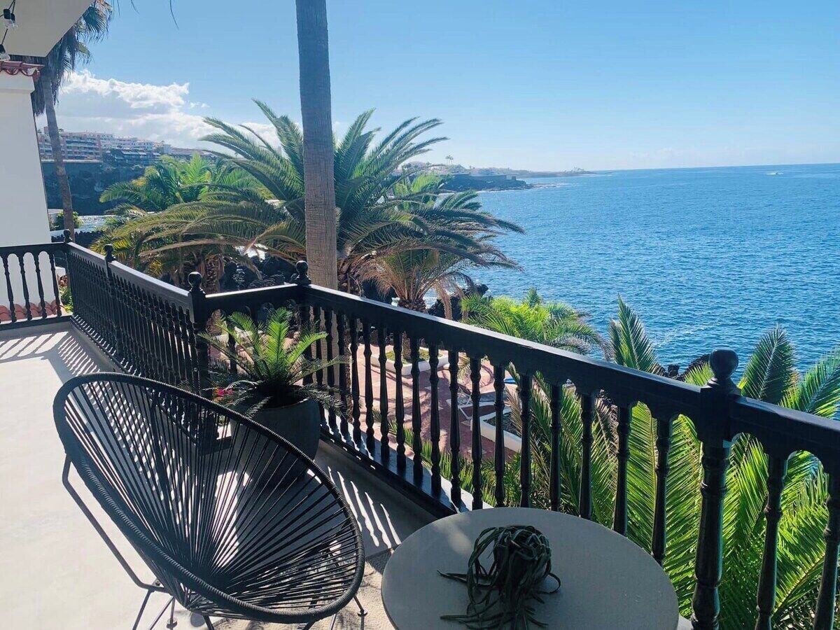Een balkon met uitzicht op zee, een palmboom en een stoel.