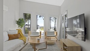Ein modernes Wohnzimmer mit einer Couch, zwei Sesseln, einem Couchtisch, einem Fernseher und großen Fenstern mit Blick.
