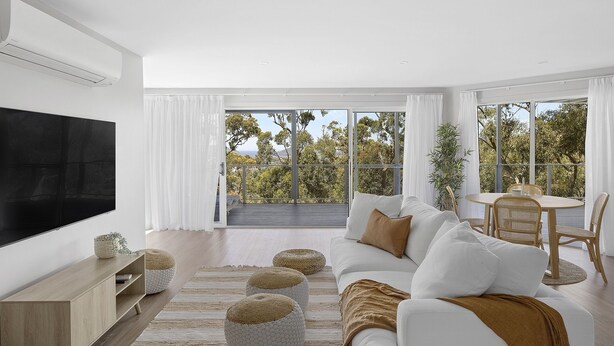 Ein modernes Wohnzimmer mit großem Fernseher, einer Couch, einem Esstisch und Blick auf Bäume durch große Fenster.
