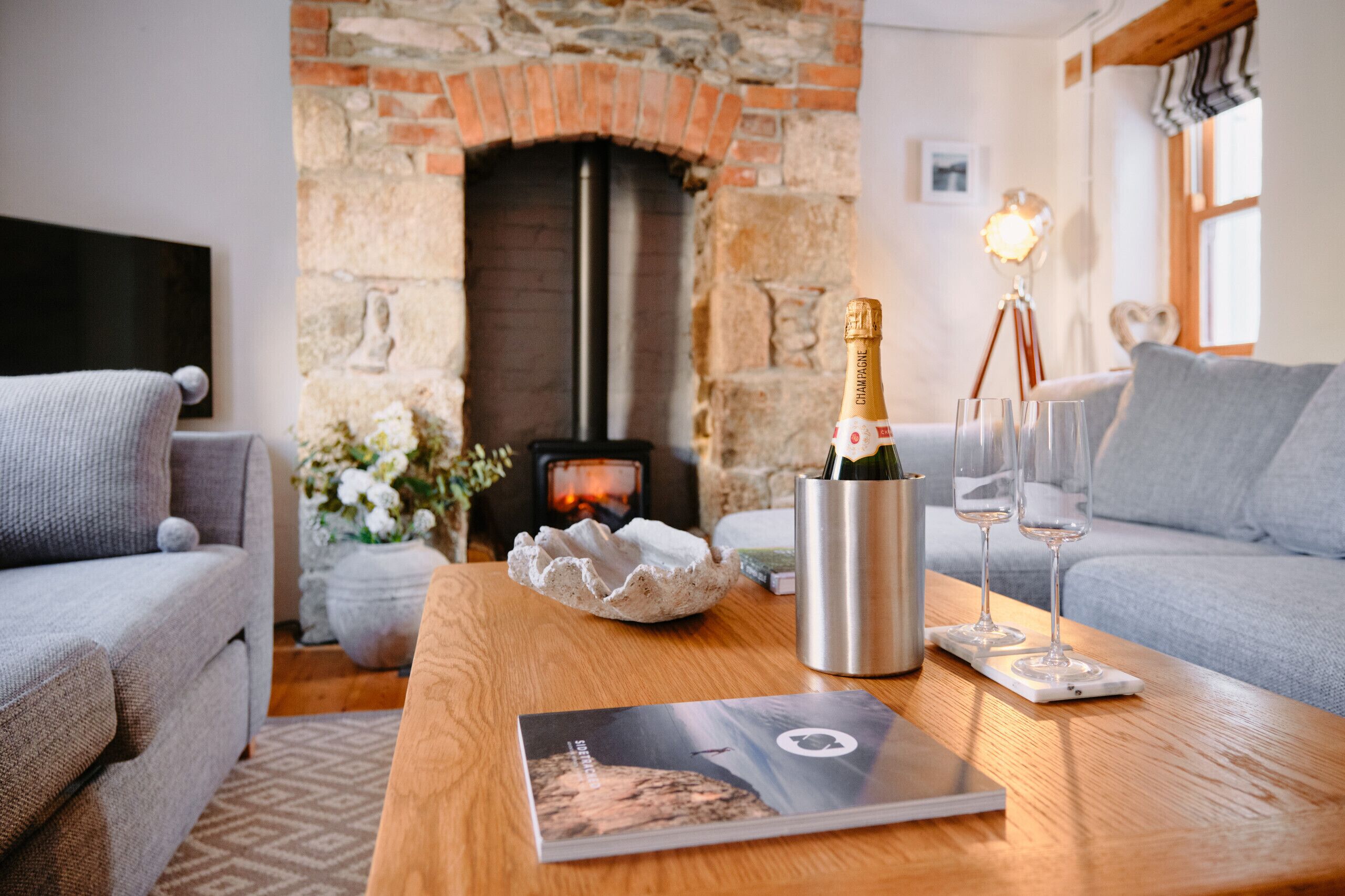 Een gezellige woonkamer met een open haard, een houten tafel met champagne, glazen en een tijdschrift.