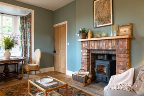 A cozy living room with a fireplace, a wicker chair, a glass coffee table, and a patterned rug.