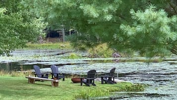 A serene lakeside setting with two Adirondack chairs and a picnic table by the water.